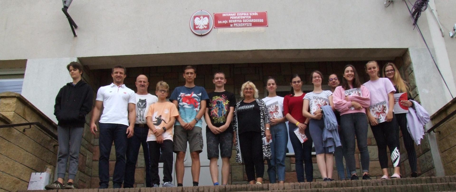Zdjęcie przedstawia grupę dzieci z Ogólnokrajowej Polskiej Szkoły na Węgrzech w Budapeszcie, opiekunkę Pani Lucyny Światłoń Szabados (w środku), wielokrotnego mistrza polski w judo Krzysztofa Wilkomirskiego (drugi od lewej) i kierownika internatu Wojciecha Włodarczyka (trzeci od lewej, w białej koszulce z wilkiem).