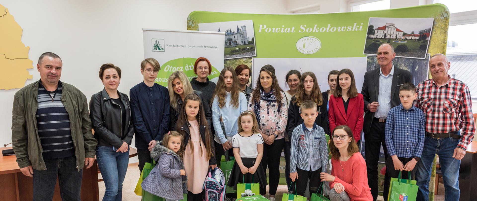 Na zdjęciu grupowym na tle banerów reklamowych KRUS i Powiatu Sokołowskiego, laureaci z nagrodami w towarzystwie rodziców, opiekunów, wicestarosty sokołowskiego oraz kierownika PT KRUS w Sokołowie Podlaskim.
