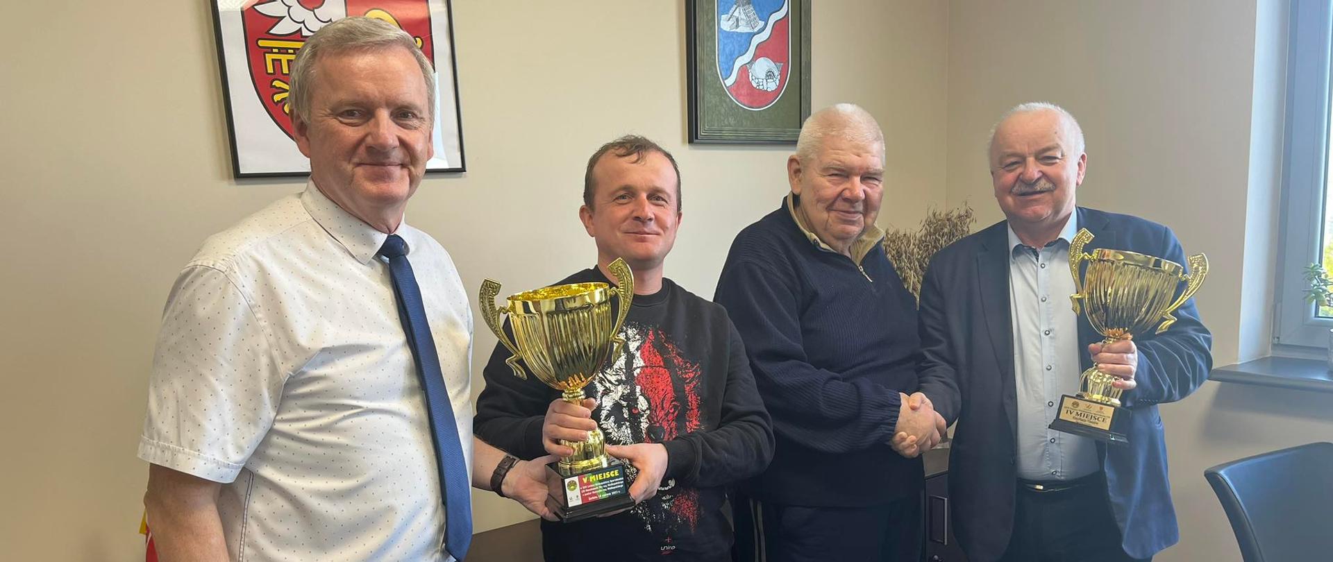 Na zdjęciu 4 mężczyzn stojących i trzymających dwa puchary 