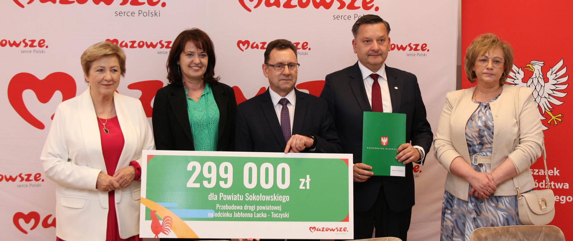 Na zdjęciu przedstawiciele województwa oraz powiatu sokołowskiego na tle ścianki z logiem Mazowsze serce polski. Starosta trzyma promesę z napisaną kwotą dofinansowania, natomiast wicestarosta teczkę z umową.