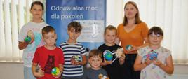 dzieci i kobieta w pomarańczowej bluzce stoją i pozują do wspólnego zdjęcia, dzieci trzymają w rękach wykonane kule z plasteliny i małe pluszaki 