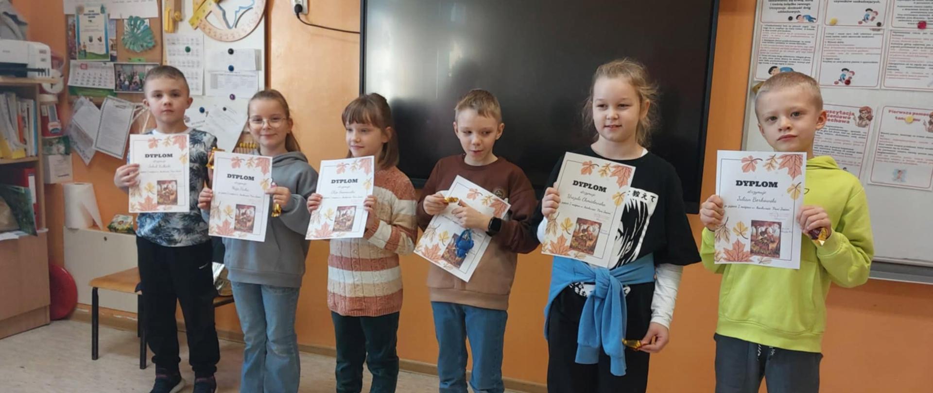 Szóstka dzieci stojąca w rzędzie. Wszyscy trzymają przed sobą oburącz dyplomy