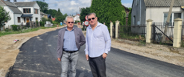 Przedstawiciele władz powiatowych na nowo wyasfaltowanym odcinku drogi, w tle widoczna zabudowa jednorodzinna oraz znaki drogowe ograniczenia prędkości.