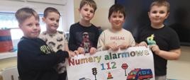 Uczniowie z klasy 2a prezentują plakat poświęcony Numerom Alarmowym