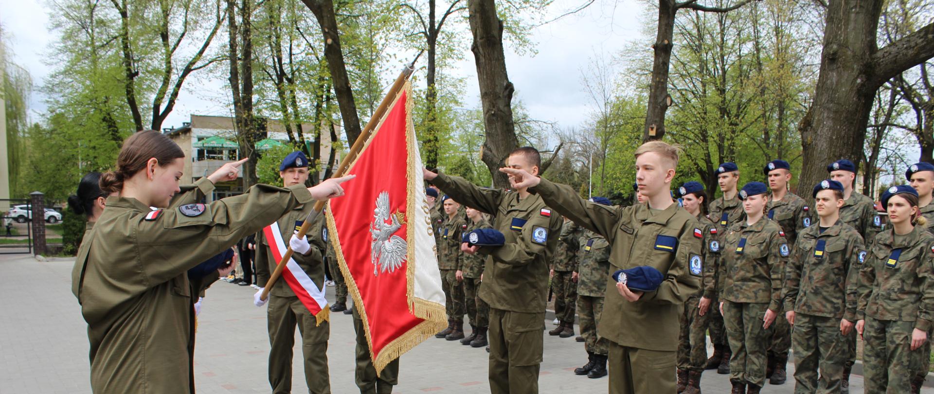 Moment składania ślubowania - przed sztandarem szkoły, stoi czterech uczniów Oddziału Przygotowania Wojskowego