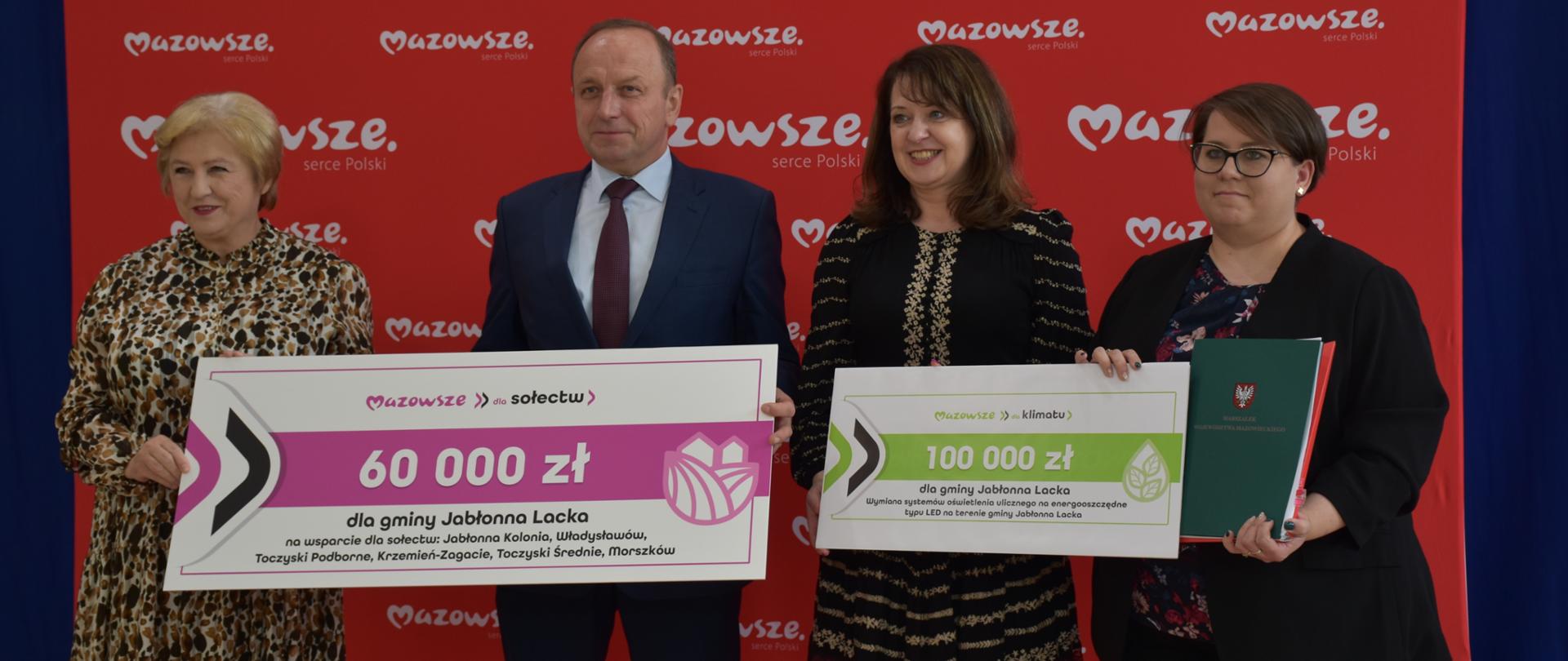 Członkowie Zarządu Województwa Mazowieckiego Janina Ewa Orzełowska i Elżbieta Lanc oraz Wójt Wiesław Michalczuk ze Skarbnik Martą Harasimiuk trzymają symboliczne tablice z kwotami dotacji.