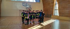 Na sali gimnastycznej Szkoły Podstawowej w Maciejowej stoją nasi zawodnicy w granatowo-zielonych koszulkach, po prawej stronie zawodnicy drużyny przeciwnej