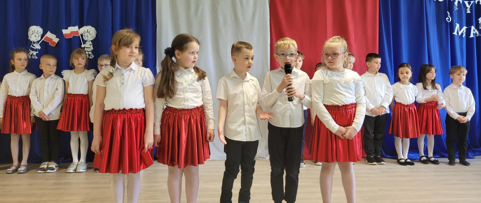 Dzieci ubrane na galowo na tle dekoracji Święto Flagi