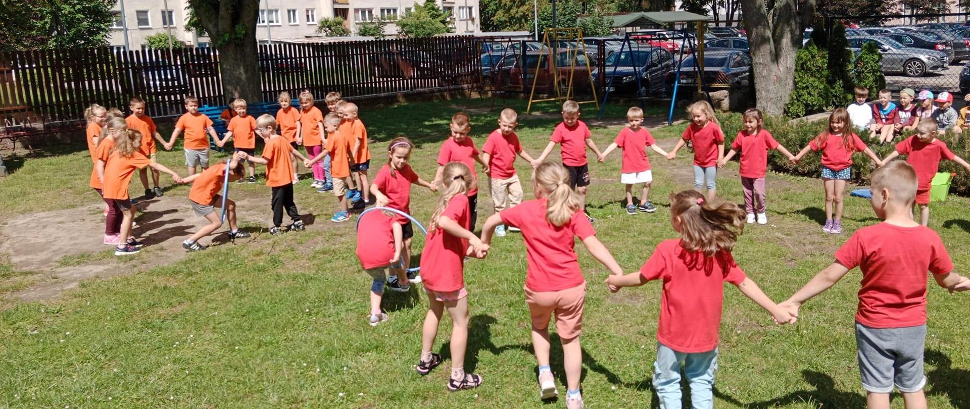Dzieci ustawione w dwóch kołach przekładają obręcz