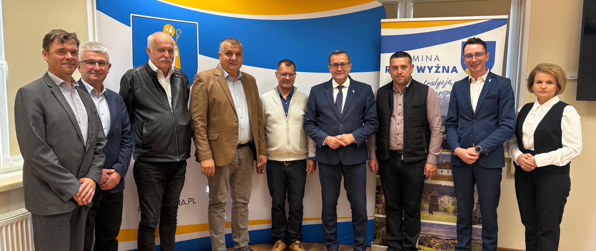 Grupowe zdjęcie uczestników spotkania na tle materiałów promocyjnych Gminy Raba Wyżna