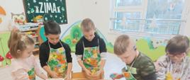 Wspólne pieczenie pierniczków - dzieci siedzą przy stole i wykonują czynności związane z przygotowaniem ciasteczek. Pozują przy tym do zdjęć