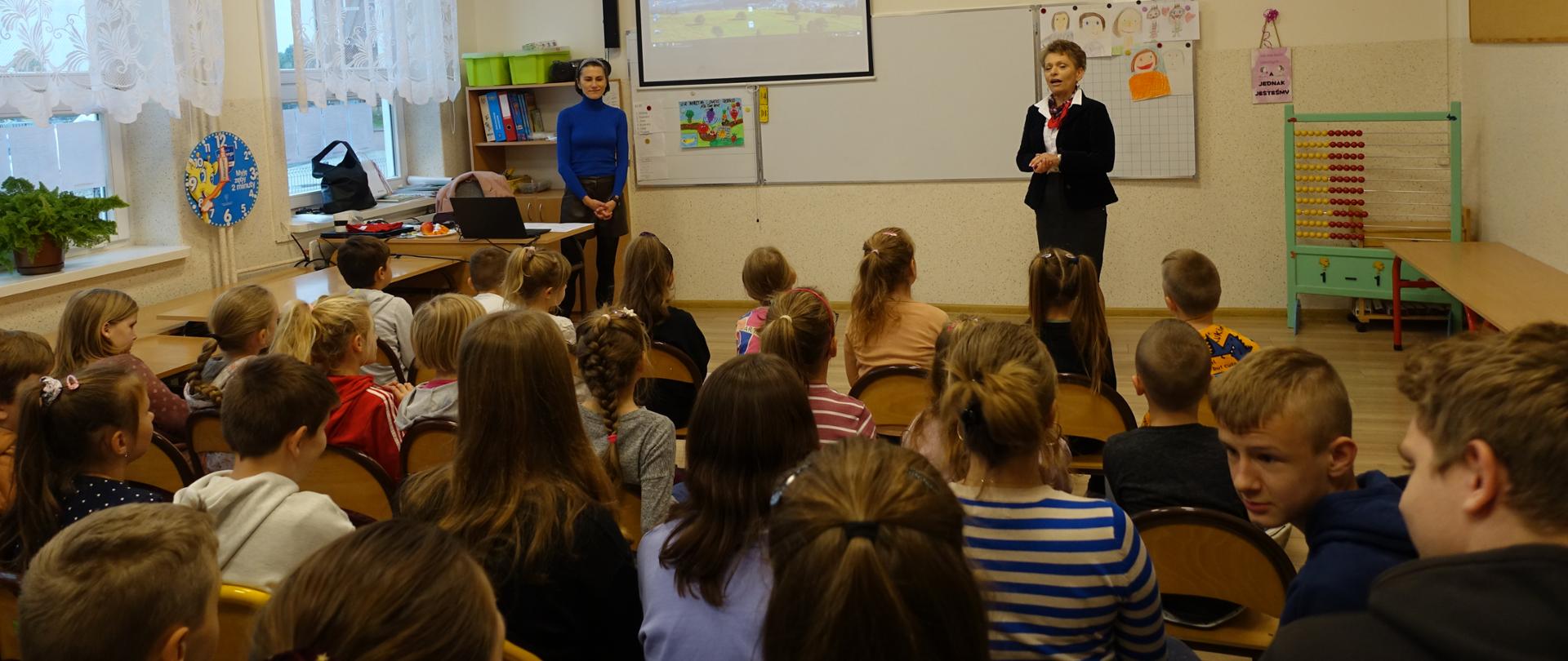 Pani Dyrektor wita panią pielęgniarkę w naszej szkole, uczniowie siedzą na krzesełkach w sali.
