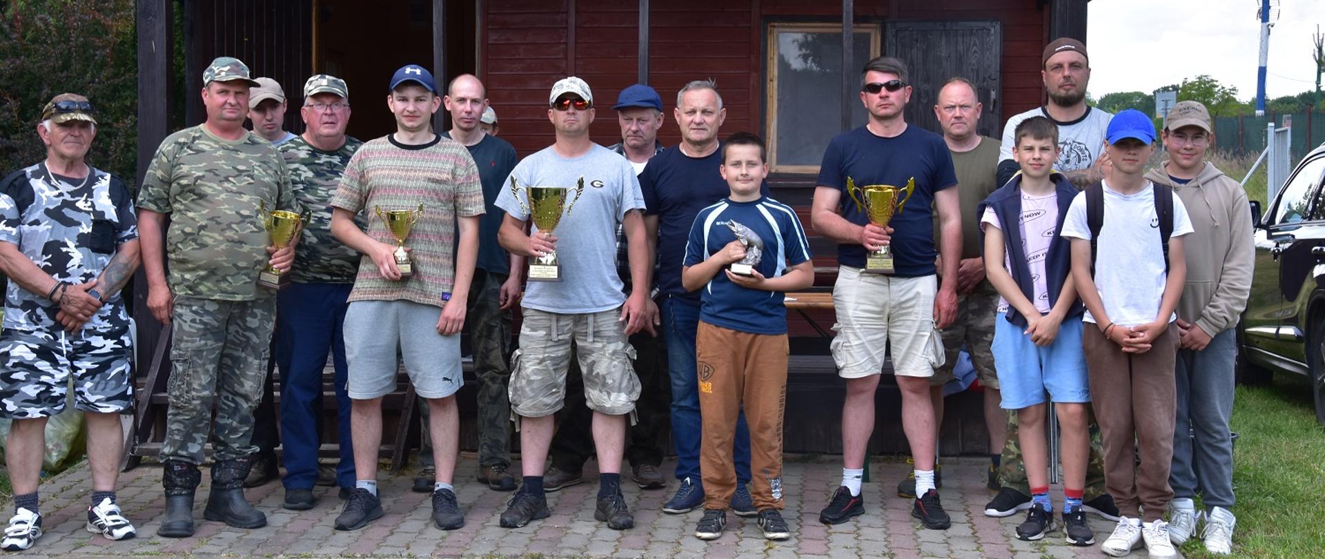 mężczyźni i dzieci pozują do wspólnego zdjęcia, czterech mężczyzn trzyma w rękach puchary jeden chłopiec statuetkę w kształcie ryby 