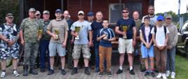 mężczyźni i dzieci pozują do wspólnego zdjęcia, czterech mężczyzn trzyma w rękach puchary jeden chłopiec statuetkę w kształcie ryby 