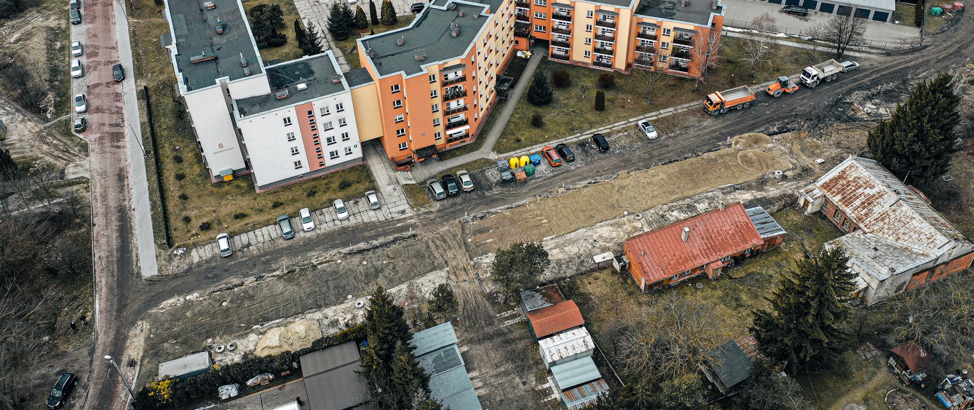 Zdjęcie przedstawia widok z drona na osiedle mieszkaniowe. Po środku remontowana i budowana droga