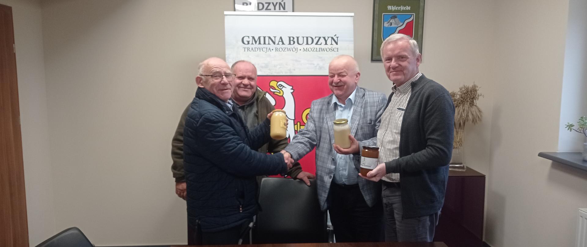 Czterech mężczyzn, dwóch przekazuje słoiki z miodem