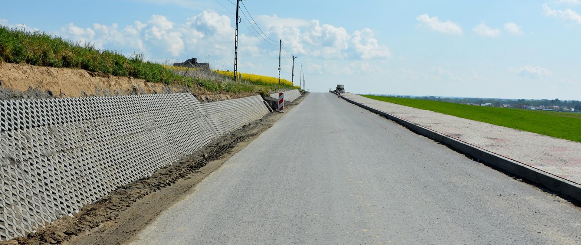 remontowana droga, z lewej strony skarpa obłożona betonowymi jumbami, z prawej strony czerwony szeroki chodnik 