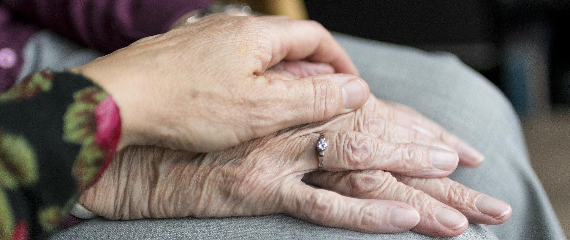 Opieka nad osoba straszą, zdjęcie symboliczne. Młodsza dłoń trzyma straszą dłoń.