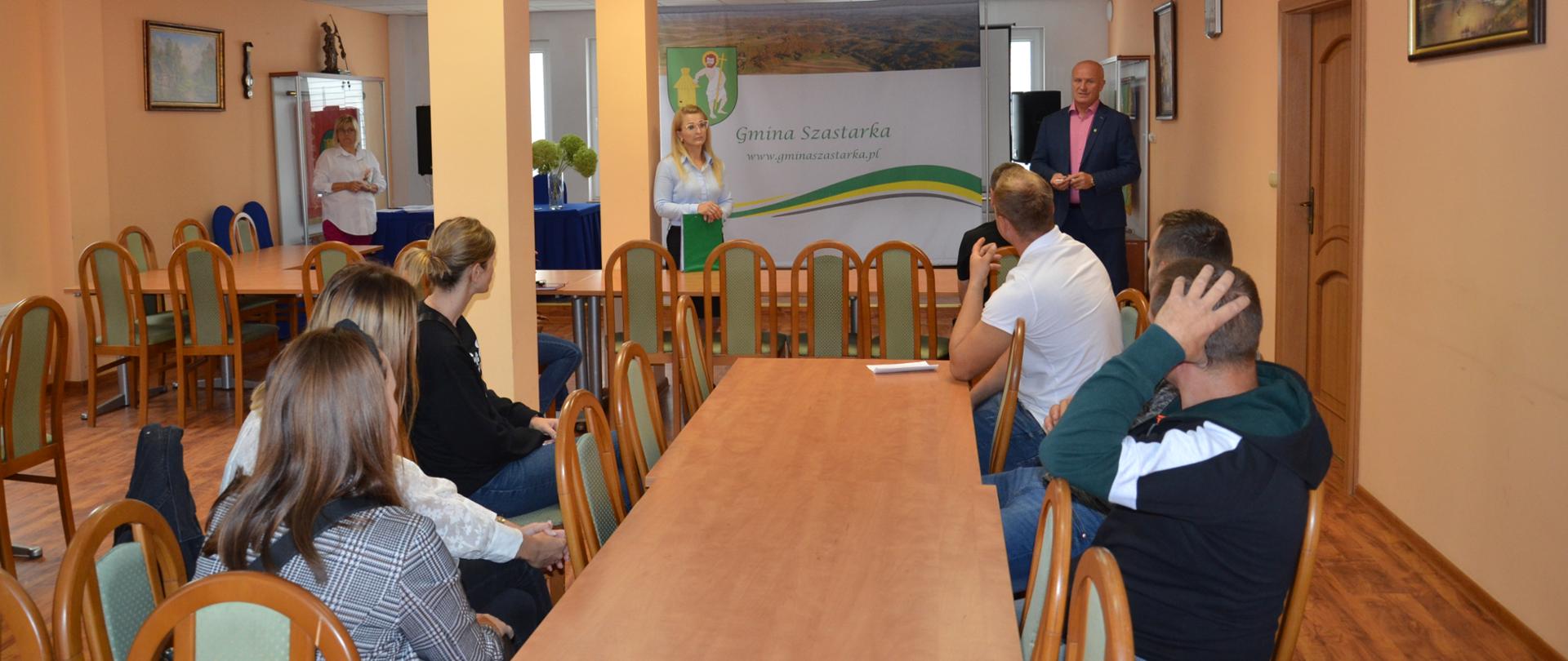 Zdjęcie przedstawia grupę ludzi siedzących przy stole słuchających Pana Wójta 