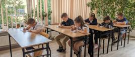 Uczniowie siedzą przy biurku, rozwiązują test