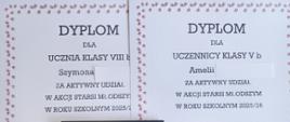 W tle dwa dyplomy, mają dookoła ramkę, czarne napisy i grafikę książek. W prawym dolnym rogu dwie karty podarunkowe. Są czarno-żółte.