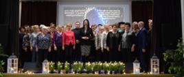 Grupa osób stoi na tle dekoracji sceny, pozując do wspólnego zdjęcia.