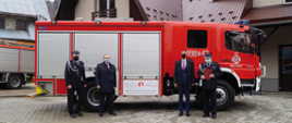 Zdjęcie przedstawiające Przedstawicieli Urzędu Gminy na tle samochodu strażackiego i remizy OSP Bielanka, przekazującego dokumenty zakupu samochodu bojowego strażakom z Bielanki. Archiwum własne