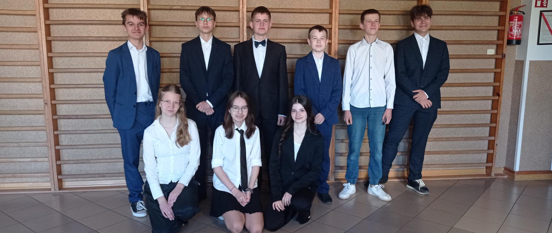 Dziewięcioro uczniów ubranych w stroje galowe pozuje do wspólnego zdjęcia.