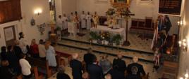 dużo ludzi stojących w kościele, ołtarz ozdobiony kwiatami, obrazy na ścianach