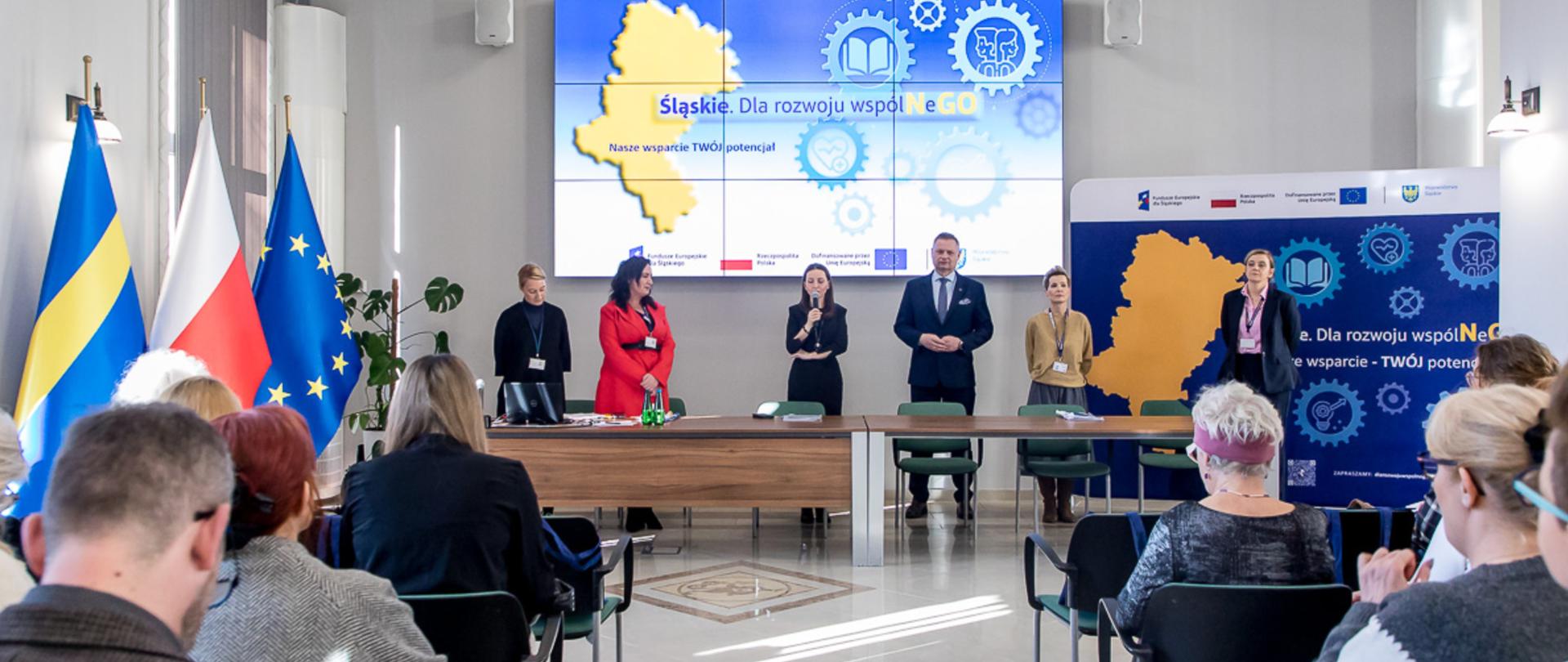 Spotkanie na sali konferencyjnej z dużą tablicą interaktywną na środku ściany