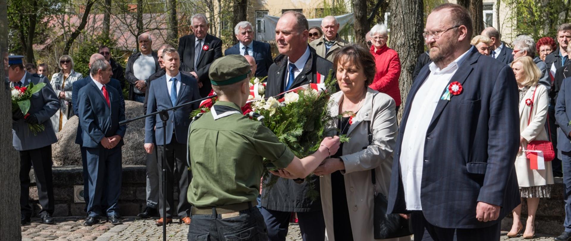 Starosta Elżbieta Sadowska przekazuje biało - czerwoną wiązankę harcerzowi celem złożenia pod pomnikiem. Wraz ze starostą stoją przewodniczący Rady Powiatu Jacek Odziemczyk oraz wicestarosta Ryszard Domański.