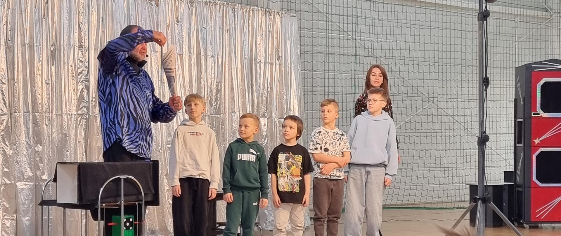 Iluzjonista wykonuje sztuczki z udziałem uczniów.