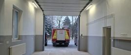 Wnętrze odnowionego garażu OSP z jasnymi ścianami, oświetleniem sufitowym i widocznym przez bramę wjazdową wozem strażackim stojącym na zewnątrz.
