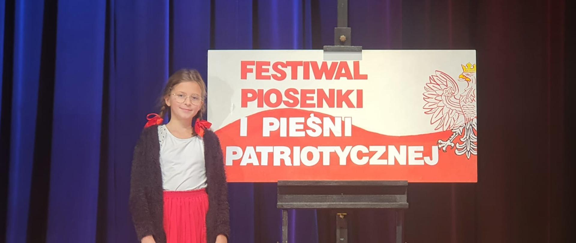 Maria pozuje przy grafice "Festiwal Piosenki i Pieśni Patriotycznej"