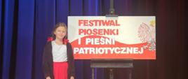Maria pozuje przy grafice "Festiwal Piosenki i Pieśni Patriotycznej"