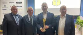 czterech mężczyzn w szeregu. Jeden trzyma puchar.