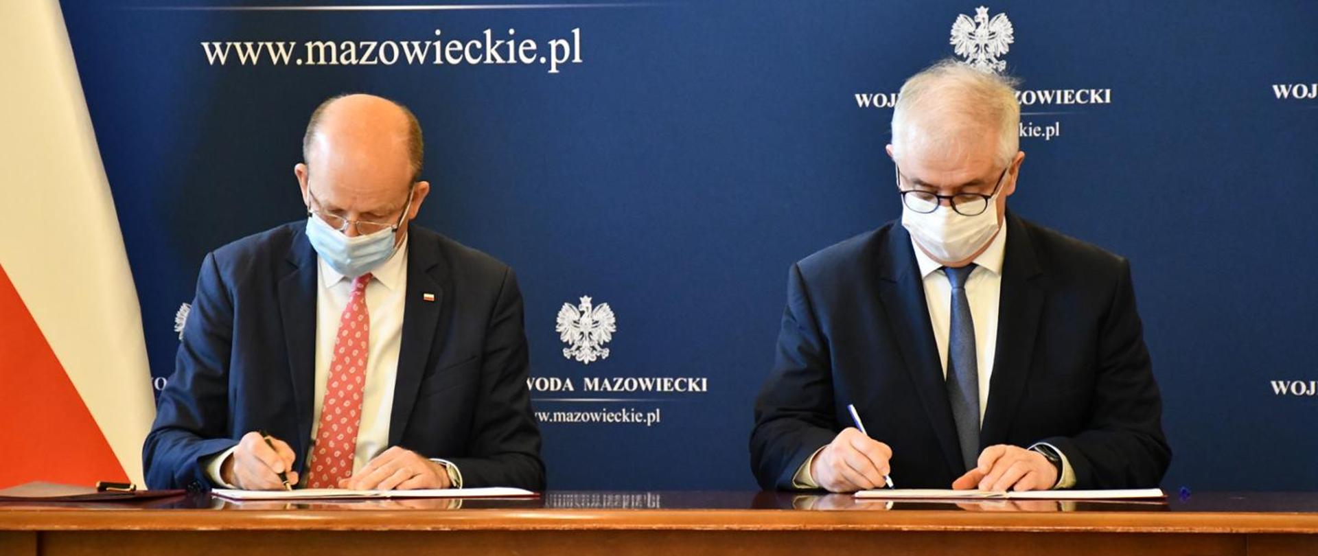 Wojewoda Mazowiecki i Starosta Pruszkowski siedzą przy stole i podpisują umowę