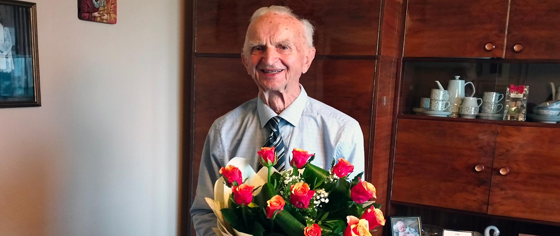 Starszy mężczyzna z bukietem kwiatów na tle brązowej meblościanki