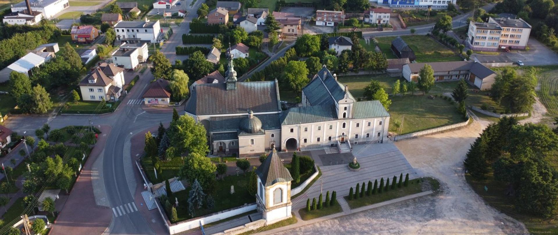 Centrum Wielgomłyn z lotu ptaka. Na pierwszym planie kościół, klasztor, dzwonnica oraz dąb pomnik przyrody. Po lewej park oraz budynki Urzędu Gminy. 