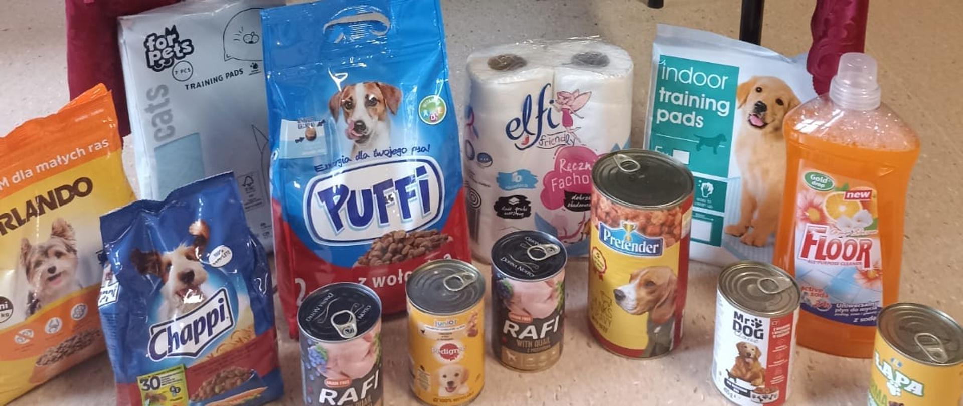 Na stoliku i pod nim zgromadzone są puszki i torby z jedzeniem dla psów zebrane przez dzieci w ramach akcji "Mam Głos"