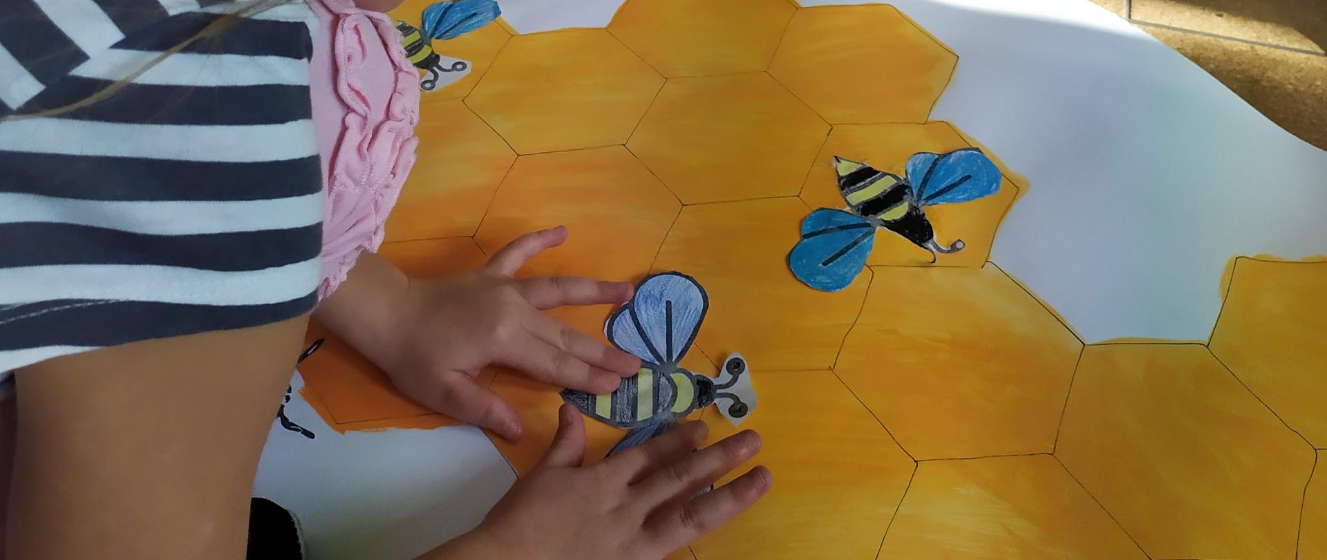 Dziewczynka przykleja obrazek pszczoły na żółty obrazek