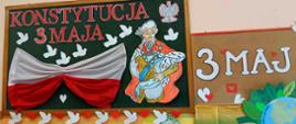 Gazetka ścienna przedstawiająca biało-czerwony napis WIWAT KONSTYTUCJA 3 MAJA oraz symbole świąteczne: flagę, gołąbki, serduszka, rysunkową postać króla Stanisława Augusta Poniatowskiego w królewskim płaszczu i peruce