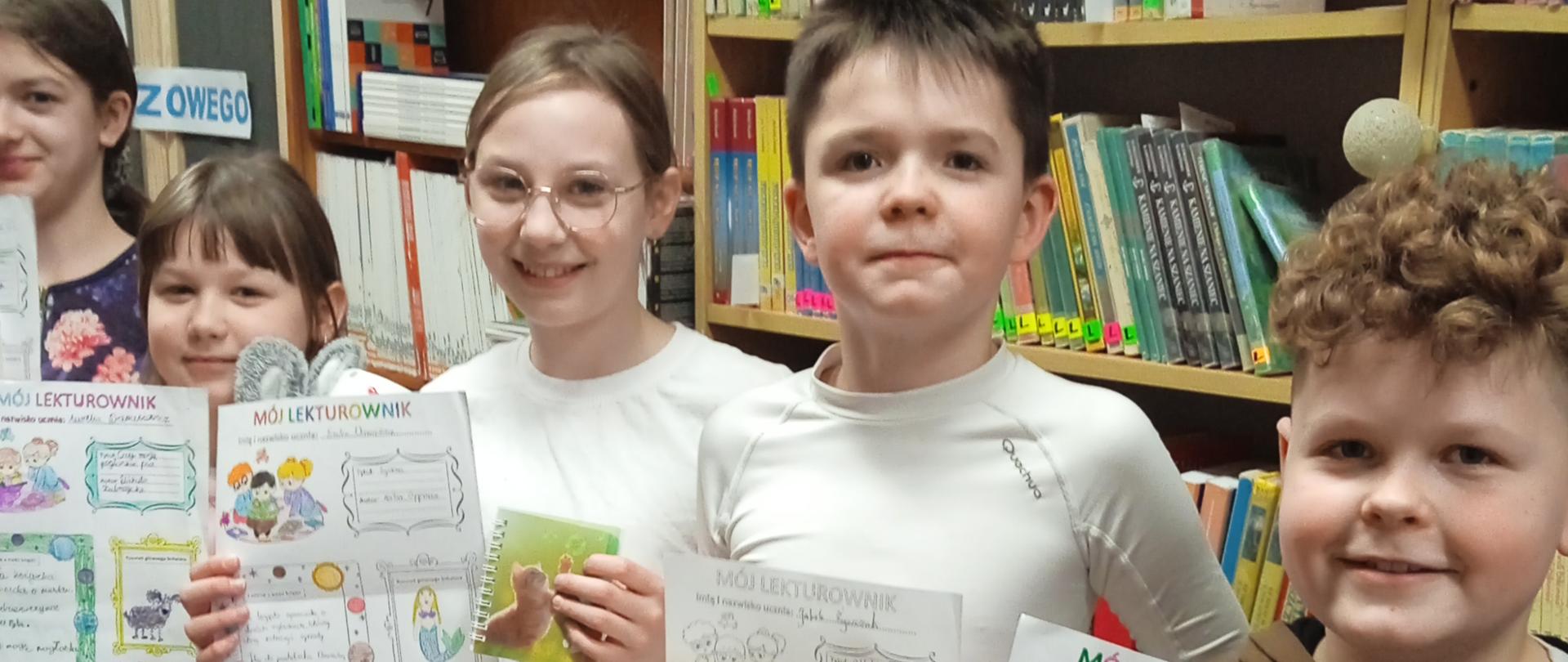 Uczniowie trzymają w ręku nagrody czyli maskotki lub kubki w kształcie zwierząt oraz ozdobione kartki lekturownika, na których opisali przeczytaną książkę