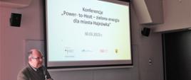 Prezentacja tematu konferencji - jeden z prowadzących przy głosie, za nim ekran z prezentacją