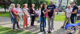 Festyn Profilaktyczno Zdrowotny w ogrodach przasnyskiego szpitala. Zdjęcie przedstawia trenerkę pomagającą starszemu mężczyźnie w wykonaniu pomiarów (w centrum). Po prawej trener personalny omawia wyniki z uczestniczką Festynu, po lewej reszta uczestników oczekuje na swoją kolej.
