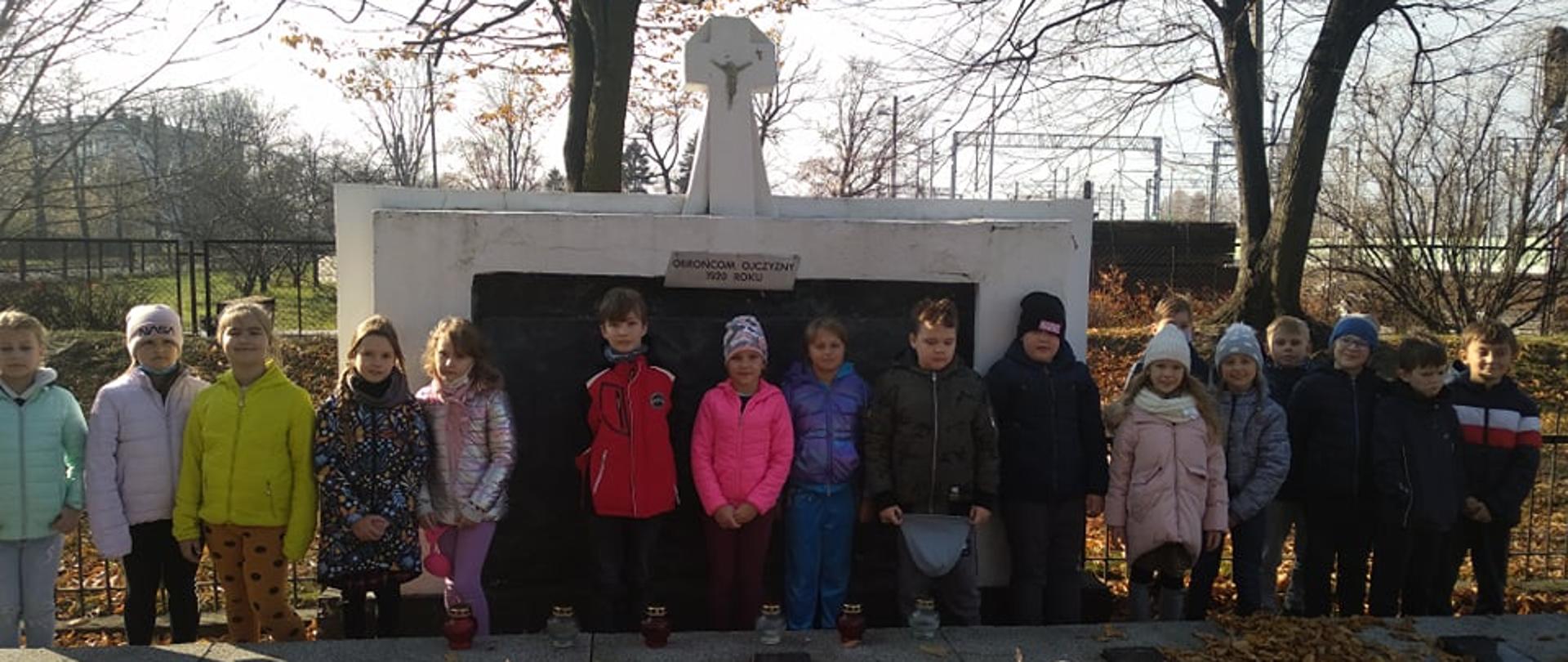 Dzieci ustawione w rzędzie pod pomnikiem