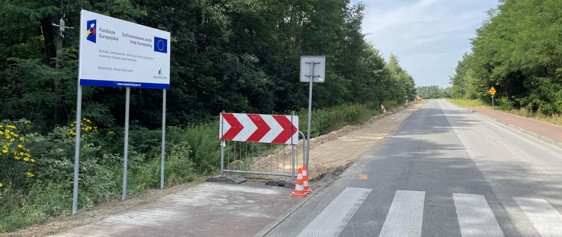 Fragment drogi powiatowej w Radgoszczy, przy której trwają prace budowlane związane z powstaniem asfaltowej ścieżki rowerowej.