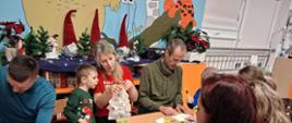 Rodzice z dziećmi siedzą przy stole, przygotowują gwiazdy z papieru