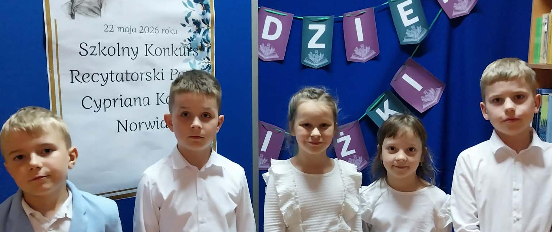 uczniowie pozują na tle plakatu informującego o udziale w szkolnym konkursie recytatorskim