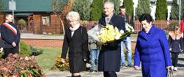Wójt Wiesław Przybylski oraz radne Hanna Zagożdżon i Jadwiga Uchal idący złożyć kwiaty pod pomnik Św. Jana Pawła II